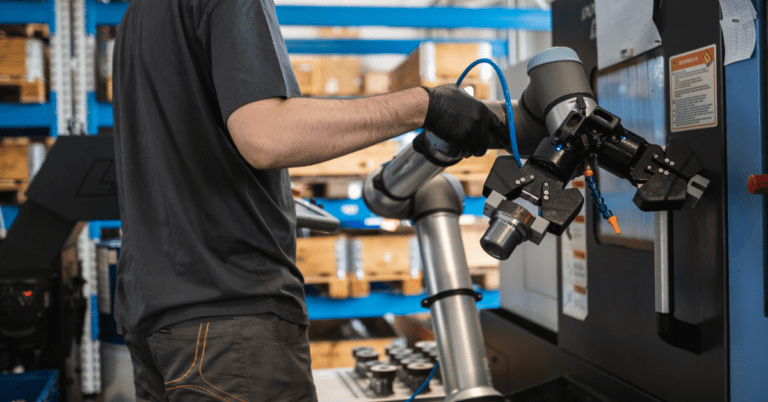 Un operario ajusta un cobot realizando tareas de carga y descarga en una máquina CNC en una fábrica de mecanizado de metal.