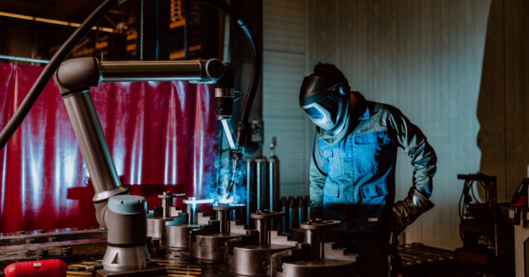 Un operario supervisa un brazo robótico colaborativo (cobot) realizando una tarea de soldadura en una fábrica de mecanizado de metal.