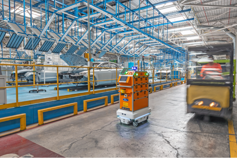 Robot móvil autónomo transportando materiales en una línea de producción automotriz.